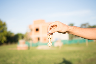 Hand holding key in front of a house in the background that is out of focus