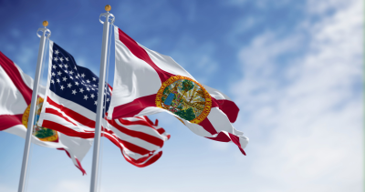 American flag and Florida state flag waving against a cloudy blue sky