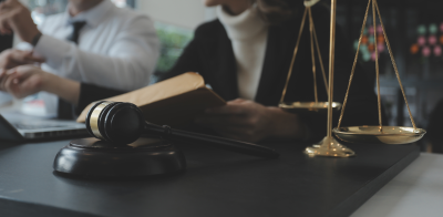 People sitting at a desk. A scales of justice and gavel are on the desk.