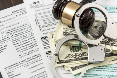 A picture of handcuffs, a gavel, and dollar bills on top of legal forms.