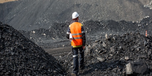Coal miner wearing safety vest and hard had in the middle of a coal field
