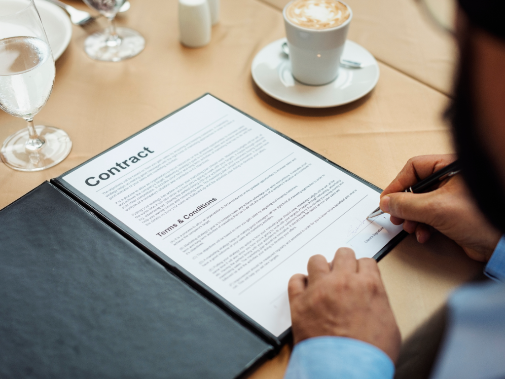 image of person signing a contract on a table next to a cup of coffee
