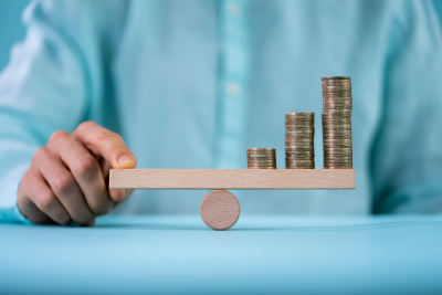 Toy sized seesaw being balanced by one finger and stacks of quarters