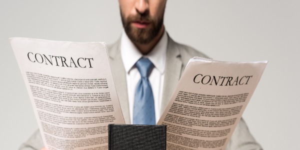 bearded man in suit and tie holding paper contracts in each hand