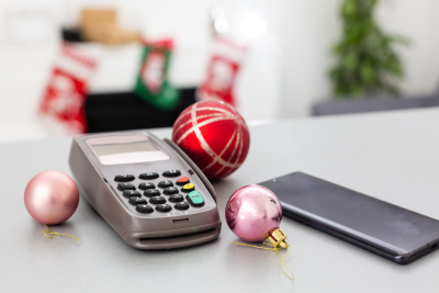 Christmas decorations and a smartphone lie next to a retail card reader on a hard surface
