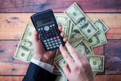 a person's hands operating a calculator over stacks of money