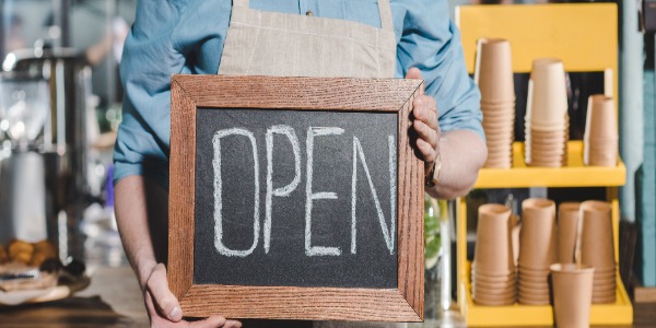 cropped-shot-of-young-male-barista-holding-chalkboard-with-lettering-open-in-coffee-shop