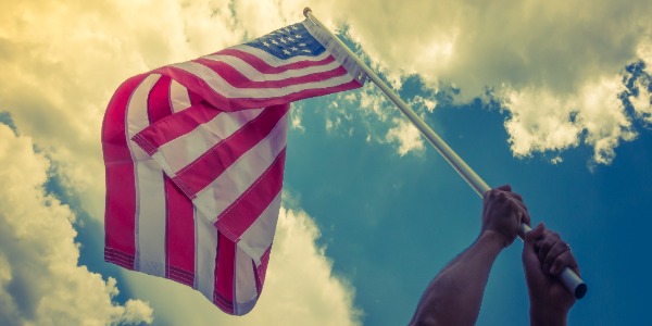 american-flag-with-stars-and-stripes-hold-with-hands-against-blue-sky-