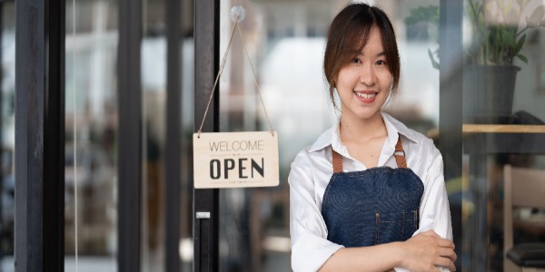 asian-young-barista-woman-in-apron-holding-tablet-and-standing-in-front-of-the-door