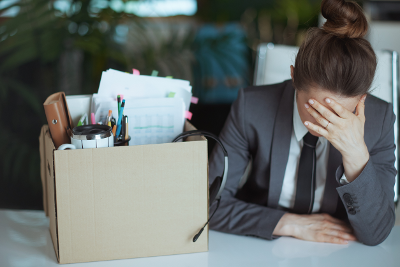 exasperated office worker with hand on face, next to a box of what are presumably their personal belongings